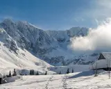Zimowy krajobraz Tatr z ośnieżonymi szczytami, chatkami i śladami na śniegu.