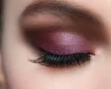 Maquillaje de ojos con sombra morada brillante y pestañas largas, ideal para realzar la mirada en párpados caídos.