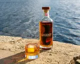 Legent Bourbon Whisky: Ein Glas und eine Flasche stehen auf einem Stein am Wasser. Was ist Bourbon Whisky? Ein Genuss für besondere Momente.