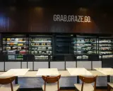 Refrigeradores llenos de comidas listas para llevar. El letrero "GRAB, GRAZE, GO" inspira una comida rápida y deliciosa.