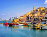 Bunte Boote im Hafen von Tel Aviv, mit der historischen Altstadt im Hintergrund und modernen Hochhäusern am Horizont.