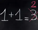 Na czarnej tablicy napisano kredą: 1+1=2. Liczba 3 jest przekreślona, jakby to był trudny egzamin dojrzałości.