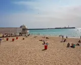 Sonniger Cadiz Strand mit Menschen, die sich am Meer entspannen. Ein weißes Gebäude mit Kuppel steht am Ufer.