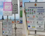 Cartelli informativi su una spiaggia libera attrezzata a Rimini, con regole per il distanziamento sociale e l'uso degli spazi.