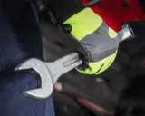 Mano con guante de alta visibilidad, parte de material de protección laboral, sujetando una llave inglesa.