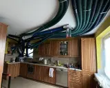 Instalacja rekuperacji w starym domu. W kuchni na suficie widać gęstą sieć zielonych i niebieskich rur wentylacyjnych.