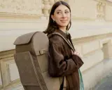 A woman smiles, showcasing the latest backpacks trend with a stylish, taupe backpack.