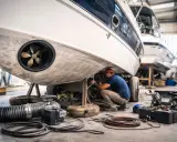 Un mécanicien travaille sur le propulseur d'étrave d'un bateau dans un atelier. Des outils et des câbles sont disposés au sol.