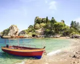 Ein Boot liegt im kristallklaren Wasser vor einer felsigen Insel mit üppiger Vegetation. Das sizilien wetter im oktober ist perfekt für einen entspannten Tag am Strand.