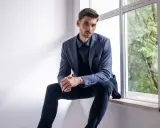 Elegancki mężczyzna w granatowej koszuli i marynarce, zastanawia się, jakie spodnie do niebieskiej koszuli będą najlepsze.
