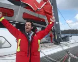 Un marinier en veste rouge célèbre sur un voilier. Une opportunité unique : ce voilier est à donner gratuitement !