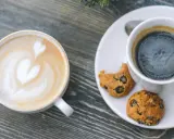 Zwei Tassen Kaffee: ein Latte mit Herz und ein starker Americano mit Keksen.