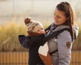 Uśmiechnięta mama z dzieckiem w nosidle, gotowi na wyprawę w góry.