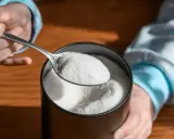 Łyżka białego proszku, z którego produkowany jest erytrytol, nad stołem.