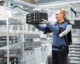 Une femme souriante porte des boîtes, aidée par un exosquelette, illustrant la définition de l'exosquelette comme aide à la manutention.