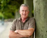 Carsten Sostmeier, ein Mann mit Brille und grauem Haar, lehnt lächelnd an einem Baum.