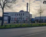 Moderne Subhan Moschee mit Minarett und Kuppel, umgeben von einem Zaun mit Schildern. Gelbe Narzissen blühen davor.