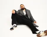 Ardalan Esmaili sitter avslappnat i en grå rock, vit skjorta och svarta byxor. Hans sneakers har en unik design.