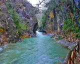 Un río turquesa serpentea entre cañones rocosos, con un sendero de madera que acompaña el recorrido. Ideales para rutas senderismo Jaén.