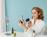 Kobieta w szlafroku sprawdza oryginalność kosmetyku za pomocą aplikacji na telefonie.