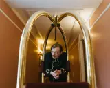 Elegancki hotelarz w historycznym mundurze czeka przy wózku bagażowym w hotelowym korytarzu.