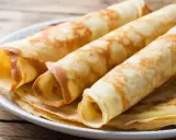 Gestapelte, gerollte Pfannkuchen ohne Mehl auf einem Teller. Sie sind goldbraun und sehen lecker aus.