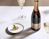 Moët & Chandon Champagnerflasche neben einem Glas Champagner und einem kleinen Häppchen. Das Etikett zeigt das Gründungsjahr, was auf den Degorgierdatum Champagner hinweist.