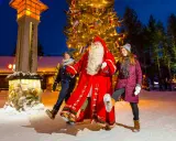 Santa Claus mit zwei Besuchern vor einem Weihnachtsbaum im Rovaniemi Weihnachtsdorf.
