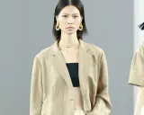 Ein Model trägt einen beigen Blazer aus knitterndem Leinen mit einem schwarzen Top. Große, runde Ohrringe schmücken ihre Ohren.