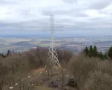Wielki metalowy krzyż góruje nad lasem na Chełmcu. W dole rozciąga się panorama miasta i pagórkowatego krajobrazu.