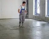 Pracownik wyrównuje świeżą wylewkę betonową na styropianie, dbając o jej minimalną grubość.