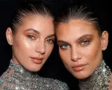 Dos mujeres con maquillaje dorado y un sutil rabillo del ojo, luciendo collares brillantes.