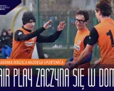 Trzech młodych piłkarzy w pomarańczowych koszulkach świętuje na boisku. Napis głosi: "Fair play zaczyna się w domu".