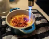 Flamme bleue caramélisant le sucre d'une crème brûlée, rappelant son origine.