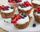 Leckere Granola Cups gefüllt mit Joghurt und garniert mit roten Johannisbeeren und Blaubeeren.