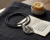 Ett silverhänge med Ganesha, om gam ganapataye namaha, på en flätad läderrem. Bredvid ligger en gammal text och ett ljus.