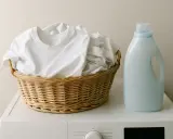 Cesta de ropa blanca lista para lavar. Detergente al lado, ideal para saber como lavar lino y mantenerlo impecable.
