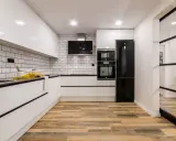 Cocina moderna con pared cocinas mitad azulejo mitad pintura blanca, electrodomésticos negros y suelo de madera.