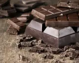 Des morceaux de chocolat noir, entiers et brisés, sur une table en bois. Une invitation à découvrir comment adoucir le chocolat noir pour une dégustation parfaite.
