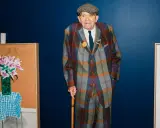 Ein Mann im karierten Anzug, inspiriert von David Hockney Pop Art, steht neben seinen lebendigen Gemälden.