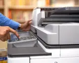 Mani che usano una stampante multifunzione, aiutando a decidere se è meglio stampante laser o inkjet per le proprie esigenze.