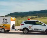 Un coche blanco de **4x4 autoescuela** con remolque, listo para enseñar a conducir en un paisaje rural.
