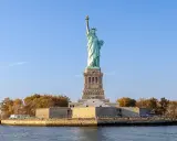 Gdzie jest Statua Wolności? Na Liberty Island, w Nowym Jorku, wznosi się dumnie symbol wolności, otoczona jesiennymi drzewami i błękitnym niebem.