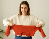 Kobieta trzyma pomarańczowy sweter, pokazując, jak uratować skurczony sweter z wełny.