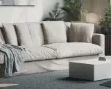 En bekväm soffa med nedsuttna dynor, prydd med en stickad pläd. Framför står ett lågt, vitt soffbord.
