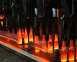 Botellas de vidrio al rojo vivo en una línea de producción, un proceso que nos recuerda quién inventó el cristal y cómo ha evolucionado.