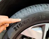 Palec wskazuje na oponę, gdzie widoczny jest rozmiar 215/60 R16. To ważny element, który określa m.in. indeks prędkości opon.