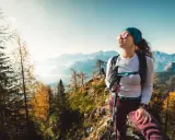 Kobieta w okularach przeciwsłonecznych i sportowym stroju, z kijkami trekkingowymi, podziwia jesienny krajobraz górski. Idealny przykład, jak się ubrać w góry.