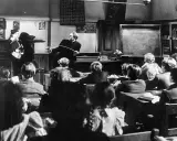Lehrer mit Stock ermahnt Schüler in einer Klasse, die an eine Schule im Mittelalter erinnert.