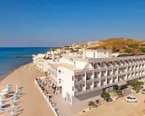 Wypoczynek na plaży w hotelu Island Maya Resort. Biały budynek hotelowy z balkonami, obok piaszczysta plaża z leżakami i parasolami, morze i wzgórza w tle.